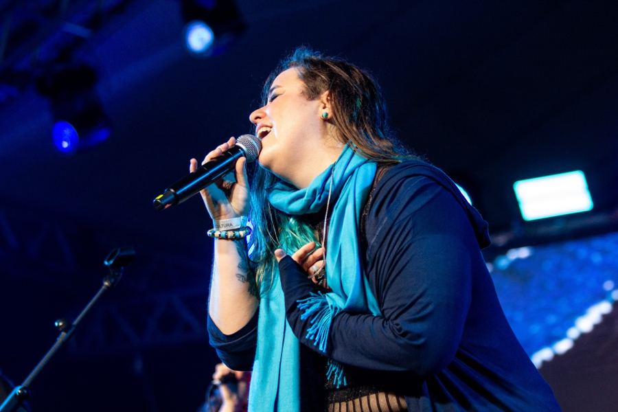 Letícia cantando de olhos fechados, com cachecol azul